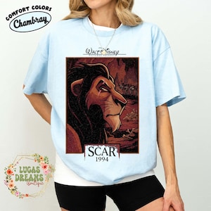 May include: A light blue t-shirt featuring a graphic print of the character Scar from The Lion King. The design includes the text Walt Disney Pictures Presents, Scar, and 1994. The shirt has a crew neckline and short sleeves, showcasing a detailed illustration of the lion against a dark, textured background with hyenas and bones.