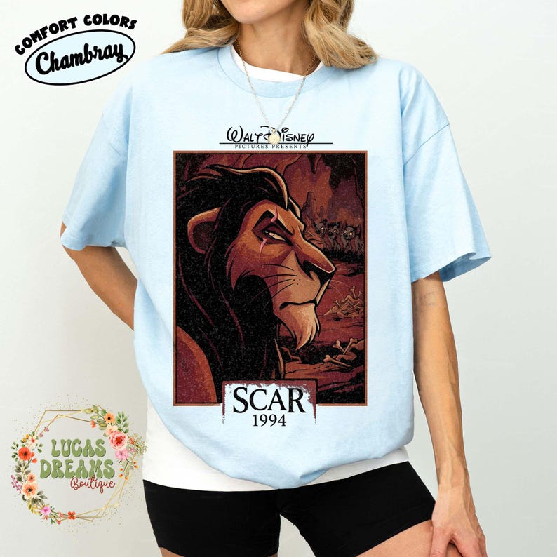 May include: A light blue t-shirt featuring a graphic print of the character Scar from The Lion King. The design includes the text Walt Disney Pictures Presents, Scar, and 1994. The shirt has a crew neckline and short sleeves, showcasing a detailed illustration of the lion against a dark, textured background with hyenas and bones.