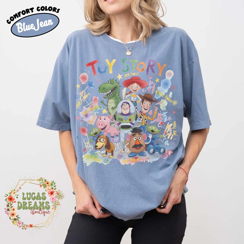 Pu&ograve; includere: T-shirt blu a maniche corte con la scritta "Toy Story" in lettere colorate e illustrazioni dei personaggi del film d'animazione. La maglietta ha un girocollo e una vestibilit&agrave; ampia. Le parole "Comfort Colors" e "Blue Jean" sono in un cerchio in alto a sinistra.