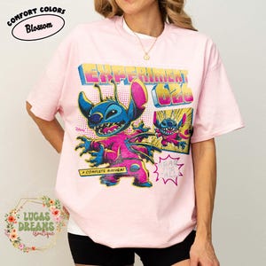 May include: Pink t-shirt featuring a graphic of Stitch from Lilo & Stitch, with the text "EXPERIMENT 626" and "A COMPLETE MAYHEM!". The shirt has a crew neck and short sleeves. The brand name "COMFORT COLORS" is printed on the top left.