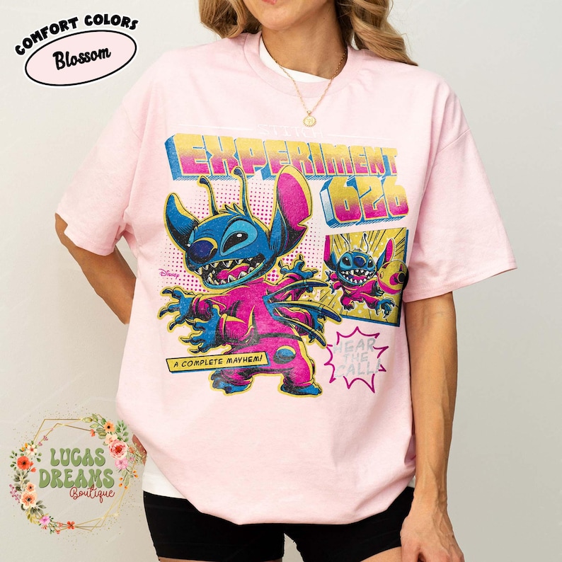 May include: Pink t-shirt featuring a graphic of Stitch from Lilo & Stitch, with the text "EXPERIMENT 626" and "A COMPLETE MAYHEM!". The shirt has a crew neck and short sleeves. The brand name "COMFORT COLORS" is printed on the top left.