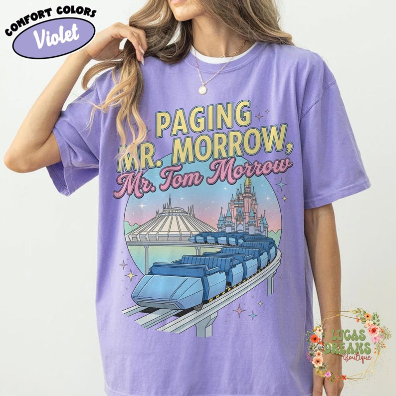 May include: Violet Comfort Colors t-shirt featuring the text "Paging Mr. Morrow, Mr. Tom Morrow" above a graphic of a roller coaster, Space Mountain, and a castle. The shirt has a crew neck and short sleeves.