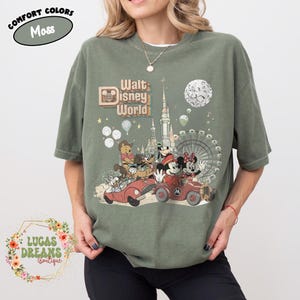 May include: Moss green t-shirt featuring a vintage-style graphic of Walt Disney World characters in cars, with a castle, Ferris wheel, and moon. The shirt includes the text "Walt Disney World" and "Comfort Colors".