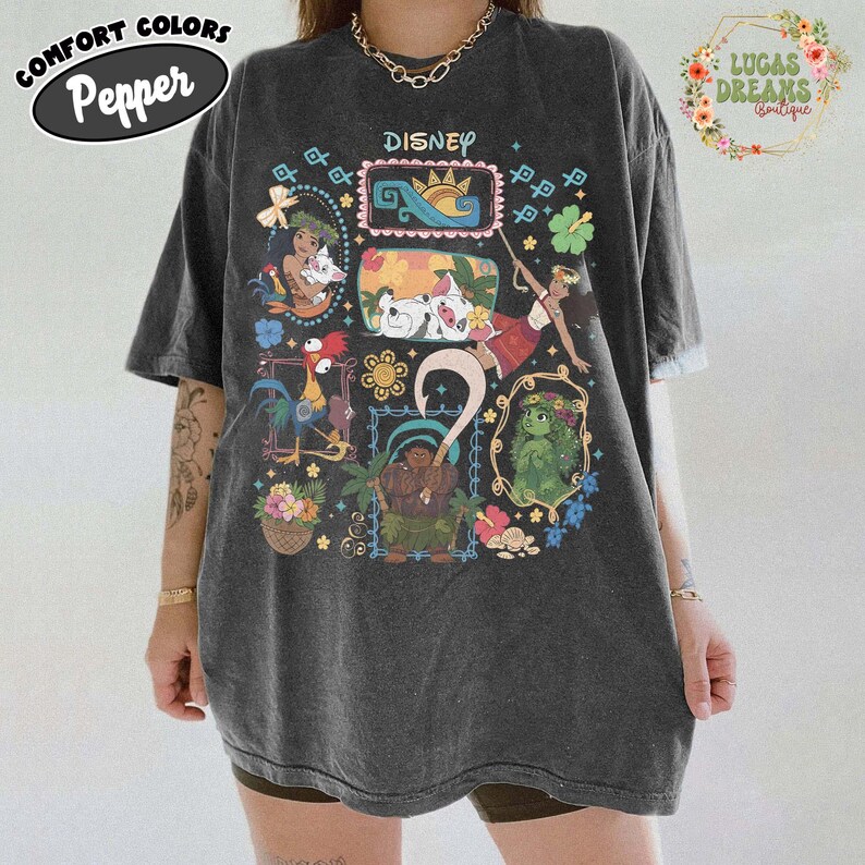 May include: Dark grey oversized t-shirt featuring Disney characters in colourful frames. The shirt has the word "Disney" printed at the top and the words "Comfort Colors Pepper" in a circular logo. The shirt is worn by a person.