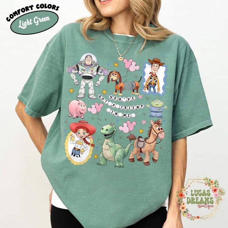 May include: Light green t-shirt featuring cartoon characters from the movie Toy Story. The shirt includes Buzz Lightyear, Woody, Jessie, and other characters. Text on the shirt reads "You've Got a Friend in Me."