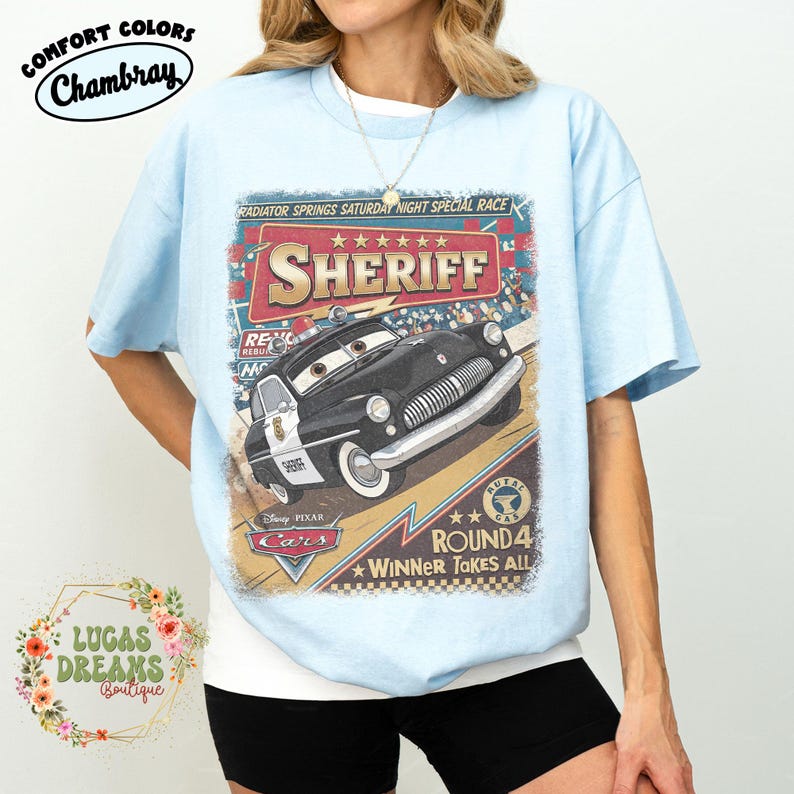 May include: Light blue t-shirt featuring a graphic of Sheriff from Disney Pixar's Cars. The design includes the text "RADIATOR SPRINGS SATURDAY NIGHT SPECIAL RACE" and "ROUND 4 WINNER TAKES ALL". The shirt has the Comfort Colors Chambray label.