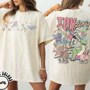 May include: Cream-coloured t-shirt with a Toy Story graphic on the front and back. The front features characters, while the back displays the Toy Story logo, characters, and the text "Since 1995."