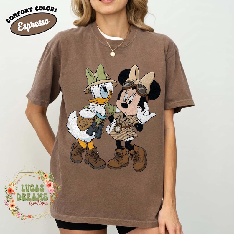 May include: Brown t-shirt with a cartoon illustration of Donald Duck and Minnie Mouse in safari outfits. The shirt has the text "COMFORT COLORS Espresso" at the top and "LUCAS DREAMS Boutique" at the bottom.