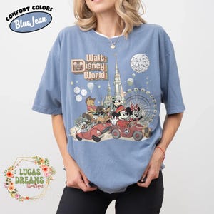 May include: Blue t-shirt with a vintage Walt Disney World graphic featuring Mickey and Minnie Mouse, Winnie the Pooh, and other characters in cars. The shirt has the text "Comfort Colors Blue Jean" and "Lucas Dreams Boutique".