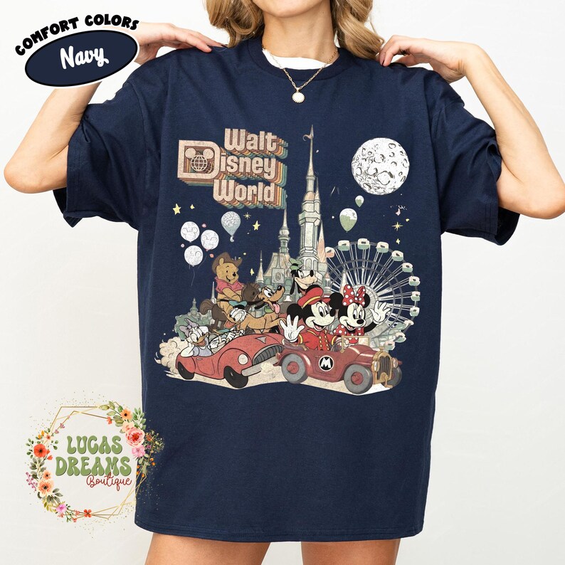 May include: Navy blue t-shirt featuring a vintage-style graphic of Walt Disney World characters in cars, with a castle, Ferris wheel, and moon. The shirt includes the text "Walt Disney World" and "Comfort Colors".