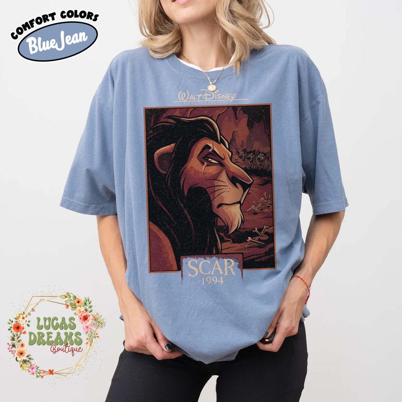 May include: A blue short-sleeve t-shirt featuring a graphic print of the character Scar from The Lion King. The design includes the text Walt Disney Presents, Scar, and 1994. The shirt has a crew neckline and a relaxed fit with a vintage-style wash.