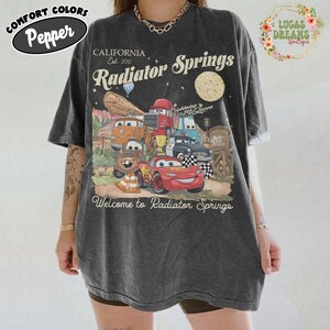 Pode incluir: Uma caneca de cer&acirc;mica branca com uma al&ccedil;a preta e o texto "But First, Coffee" em preto, em negrito. A caneca est&aacute; sobre uma superf&iacute;cie branca.