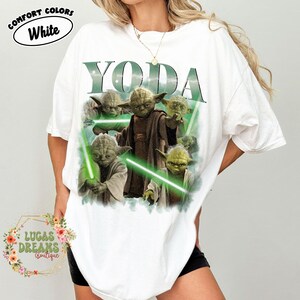 Puede incluir: Una camiseta blanca de manga corta con un estampado gr&aacute;fico del personaje Yoda en varias poses con sables de luz verdes. El texto YODA est&aacute; impreso en letras grandes de color verde oscuro sobre el personaje. Tiene cuello redondo y corte holgado.
