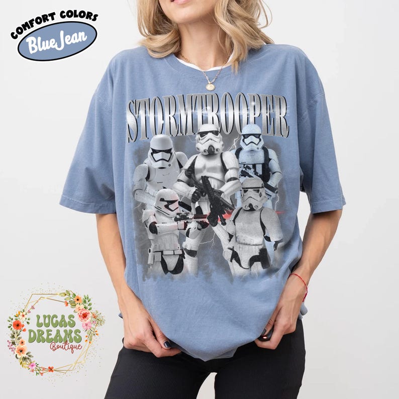 Puede incluir: Una camiseta de color azul vaquero con un estampado gr&aacute;fico de cinco soldados de asalto blancos con armadura que sostienen bl&aacute;steres. La palabra STORMTROOPER est&aacute; impresa en una fuente plateada met&aacute;lica sobre los personajes. Manga corta.