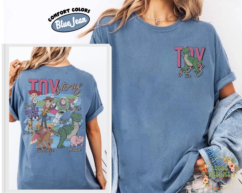 Peut inclure: T-shirt bleu jean avec un motif du film "Toy Story". Le devant pr&eacute;sente Rex le dinosaure, et le dos un motif plus grand avec des personnages et le mot "Toy Story" en rose. Marque Comfort Colors.