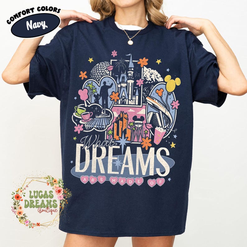 K&ouml;nnte beinhalten: Marineblaues T-Shirt mit einem farbenfrohen Grafikdesign mit ikonischen Wahrzeichen und Figuren. Der Text "What Dreams Are Made Of" ist deutlich sichtbar. Das Shirt tr&auml;gt auch die Aufschrift "Comfort Colors" und "Navy".