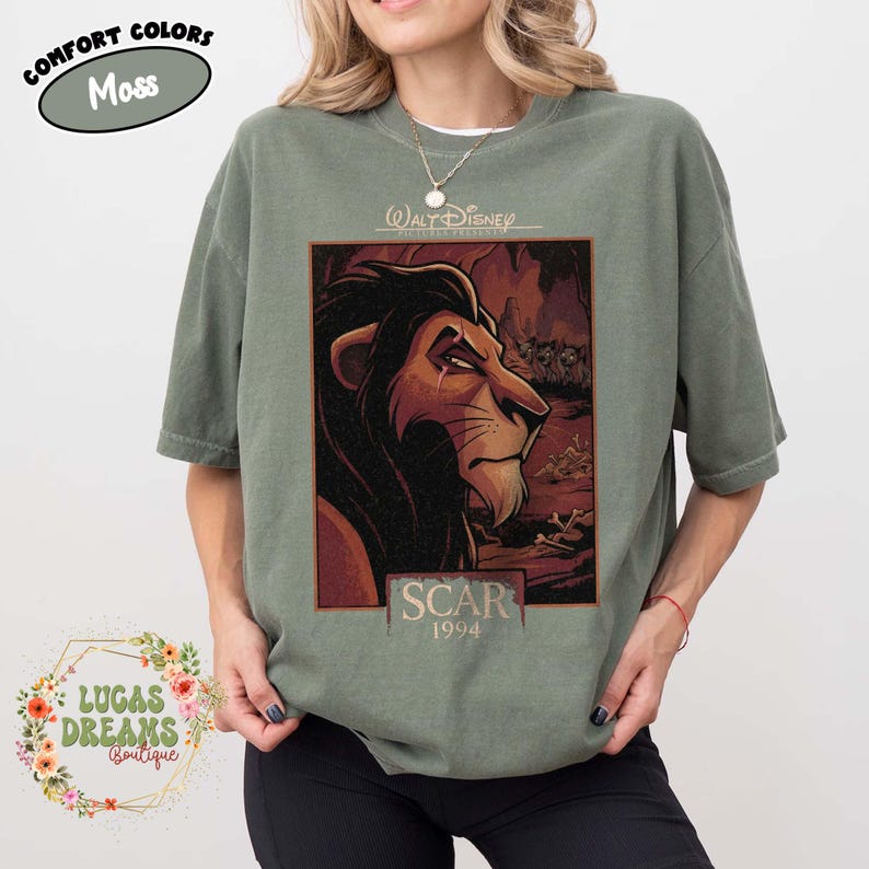 May include: A moss green short-sleeve t-shirt featuring a graphic print of the character Scar from The Lion King. The design includes the text Walt Disney, Scar, and 1994. The shirt has a crew neckline and a relaxed fit, showcasing a detailed illustration.