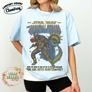 Puede incluir: Una camiseta azul claro con un gr&aacute;fico de The Mandalorian y Grogu. El texto dice STAR WARS THE MANDALORIAN, WHEN YOU CHOOSE TO WALK THE WAY OF THE MANDALORE YOU ARE BOTH HUNTER & PREY. El dise&ntilde;o incluye una insignia de cazarrecompensas.