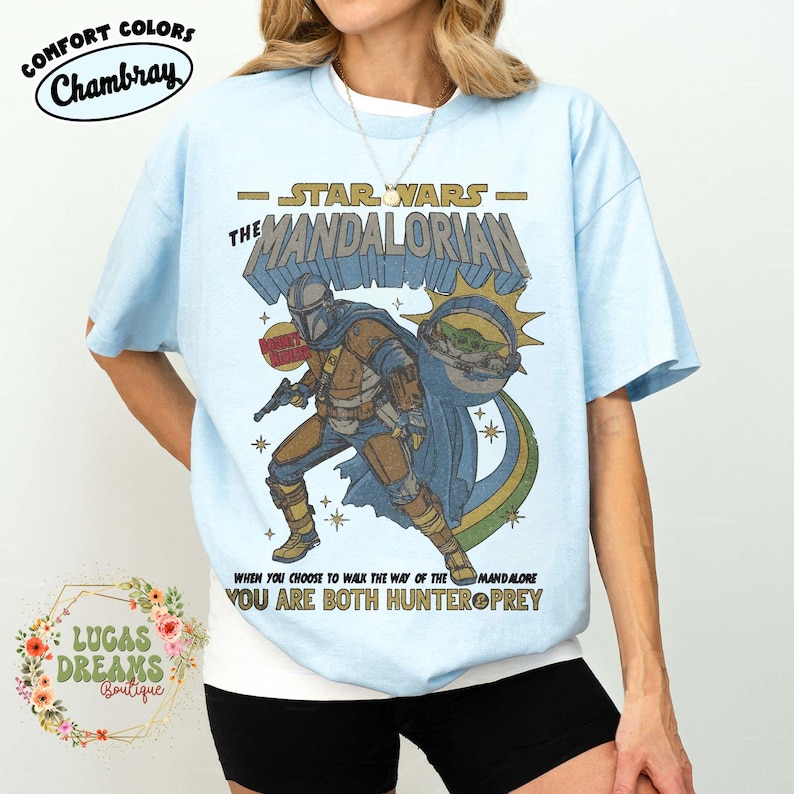 Puede incluir: Una camiseta azul claro con un gr&aacute;fico de The Mandalorian y Grogu. El texto dice STAR WARS THE MANDALORIAN, WHEN YOU CHOOSE TO WALK THE WAY OF THE MANDALORE YOU ARE BOTH HUNTER & PREY. El dise&ntilde;o incluye una insignia de cazarrecompensas.