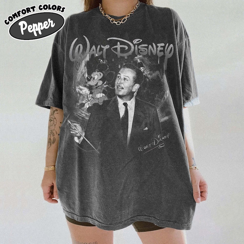 Peut inclure: Un t-shirt gris anthracite &agrave; manches courtes avec un graphisme de style vintage repr&eacute;sentant Walt Disney en costume-cravate accompagn&eacute; de Mickey Mouse. Le texte Walt Disney est imprim&eacute; en haut dans une police stylis&eacute;e, avec une signature sous le visuel. Le t-shirt est &eacute;tiquet&eacute; Comfort Colors Pepper.