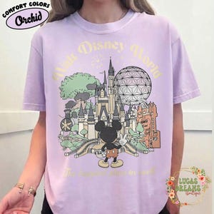 May include: Orchid Comfort Colors t-shirt featuring a vintage-style illustration of Walt Disney World. The design includes Cinderella's castle, Spaceship Earth, and Mickey Mouse. Text reads "Walt Disney World" and "The happiest place on earth."