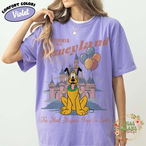 May include: Violet Comfort Colors t-shirt featuring a Disneyland graphic. The design includes Pluto, a castle, balloons, and the text "California 1955 Disneyland" and "The Most Magical Place On Earth."