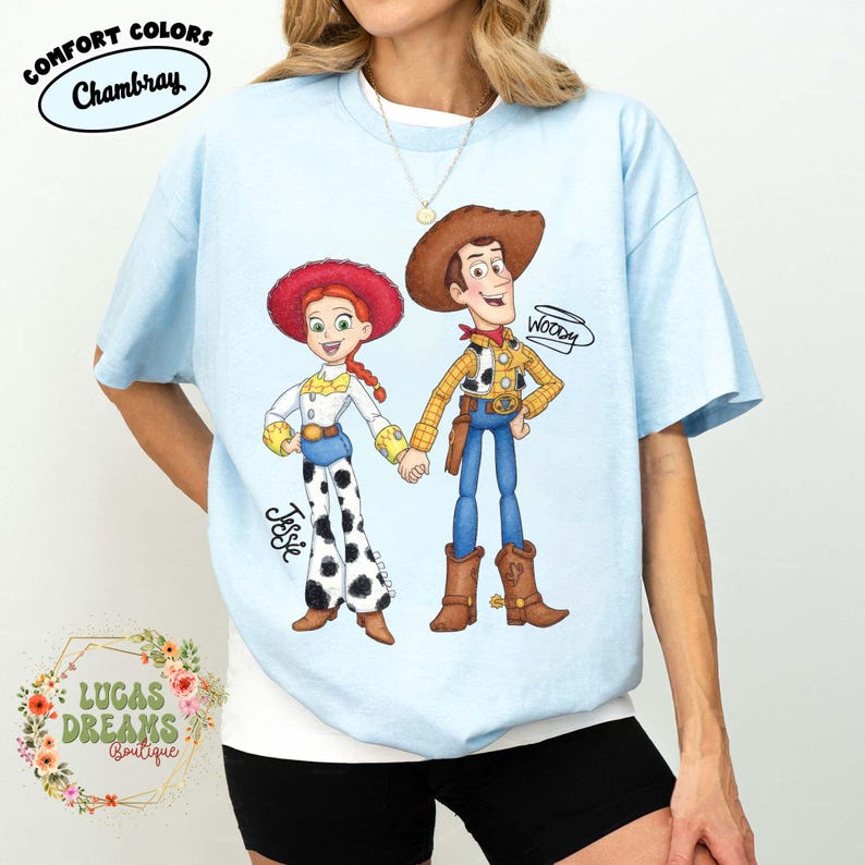 Puede incluir: Camiseta azul claro con una ilustraci&oacute;n de dibujos animados de Woody y Jessie de Toy Story. Woody lleva un sombrero de vaquero y Jessie tiene un sombrero rojo. La camiseta tiene el texto "Comfort Colors Chambray" y "Lucas Dreams Boutique".