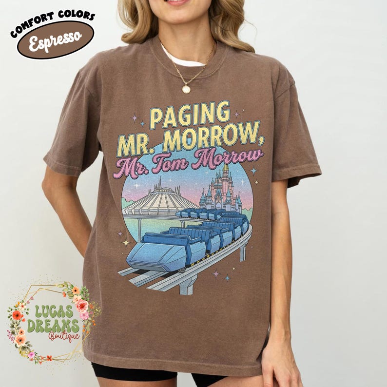 May include: Brown t-shirt featuring the text "Paging Mr. Morrow, Mr. Tom Morrow" and a graphic of a futuristic ride with a castle and space mountain in the background. The shirt also has the words "Comfort Colors Espresso" in a circle.