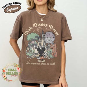 May include: Espresso-colored t-shirt featuring a Walt Disney World graphic with Mickey Mouse, a castle, and the text "The happiest place on earth." The shirt also has the text "Comfort Colors."