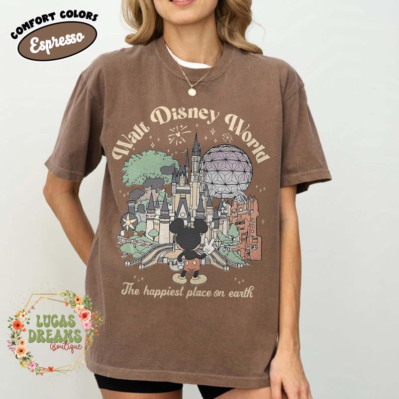May include: Espresso-colored t-shirt featuring a Walt Disney World graphic with Mickey Mouse, a castle, and the text "The happiest place on earth." The shirt also has the text "Comfort Colors."