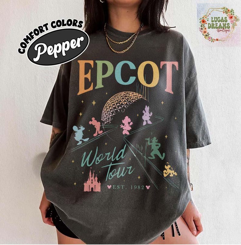 Puede incluir: Camiseta gris oscuro con la palabra "EPCOT" en letras coloridas. La camiseta presenta un gr&aacute;fico de la esfera EPCOT, personajes de Disney y las palabras "World Tour" y "Est. 1982". La camiseta est&aacute; etiquetada como "Comfort Colors Pepper".