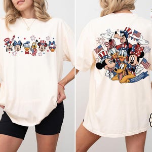 以下が含まれることがあります： アイボリー色のTシャツ。前面には花火とキャラクター、背面にはアメリカ国旗を持ったキャラクターが描かれた愛国的なデザイン。ゆったりとしたフィット感のTシャツです。