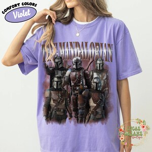 Puede incluir: Una camiseta violeta de manga corta con un estampado gr&aacute;fico de cinco personajes Mandalorianos con armadura. El texto THE MANDALORIAN est&aacute; impreso en una fuente met&aacute;lica sobre los personajes. La camiseta tiene un cuello redondo.