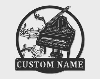 Può includere: Un'insegna da parete in metallo nero raffigurante la sagoma di un pianoforte a coda circondata da note musicali e pentagrammi all'interno di una cornice circolare. Sotto il cerchio, una targa rettangolare mostra il testo CUSTOM NAME in maiuscolo.