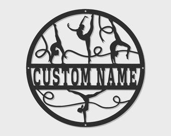 May include: A circular black metal wall sign featuring silhouettes of four gymnasts performing various poses with ribbons. A horizontal bar across the center contains the text CUSTOM NAME in bold, capital, sans-serif letters. The design includes small mounting holes.