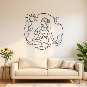May include: A black metal wall art piece featuring a continuous line drawing of a person in a seated yoga pose. The design includes a sun, a crescent moon, and a small plant with leaves, all enclosed within a fluid, organic circular outline.