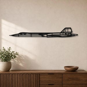 Op de afbeelding: Een zwart metalen wanddecoratie in de vorm van het silhouet van een SR-71 Blackbird vliegtuig. Het ontwerp heeft een lang, gestroomlijnd lichaam met een spitse neus, een duidelijk cockpitgedeelte en een platte, langwerpige staartstructuur.