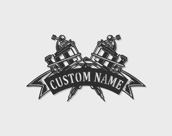 May include: A black and white graphic illustration featuring two crossed tattoo machines positioned behind a curved banner. The banner contains the text CUSTOM NAME in a bold, capitalised, serif font. The design uses high-contrast shading.