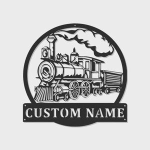 May include: Black metal train silhouette with a circular frame and the text "CUSTOM NAME" on a rectangular plate. The train features a detailed design of a locomotive, cars, and smoke. Ideal for personalized home decor.