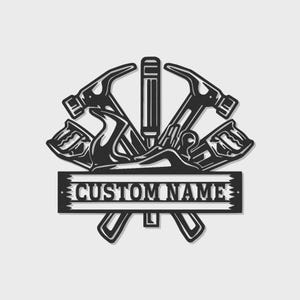 Może przedstawiać: Czarne metalowe logo stolarza z skrzyżowanymi młotkami, strugiem i dłutem. Projekt zawiera prostokątny baner z napisem "CUSTOM NAME". Ozdobny emblemat dla entuzjastów obróbki drewna.