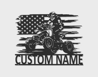 May include: A black metal wall art piece featuring a silhouette of a person riding an ATV in front of a distressed American flag design. Below the graphic, a horizontal bar contains the text CUSTOM NAME in bold, capital, sans-serif lettering.