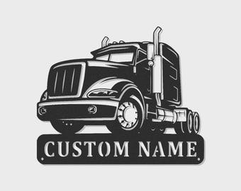 Op de afbeelding: Een zwart-wit metalen wandbord met een gedetailleerde illustratie van een vrachtwagen. De truck is afgebeeld vanuit een vooraanzicht met een prominente grille en uitlaatpijp. Onder de truck bevindt zich een plaat met de tekst CUSTOM NAME.