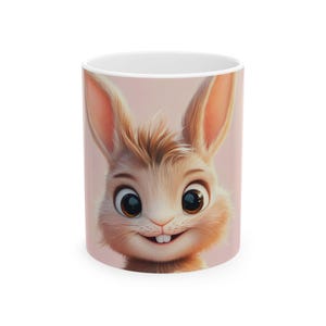 Può includere: Tazza in ceramica bianca con un design a coniglietto dei cartoni animati. Il coniglietto ha grandi occhi, un sorriso allegro e una pelliccia marrone chiaro. Lo sfondo della tazza è rosa chiaro. Un design affascinante e allegro.