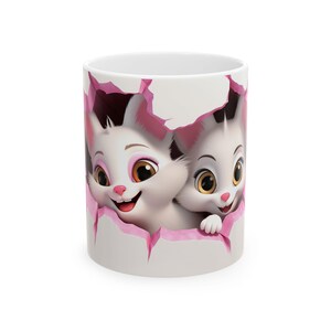 Può includere: Tazza in ceramica bianca con un'illustrazione a cartoni animati di due gattini bianchi che sbucano da un buco bordato di rosa. I gattini hanno grandi occhi e sorridono. La tazza è di dimensioni standard.