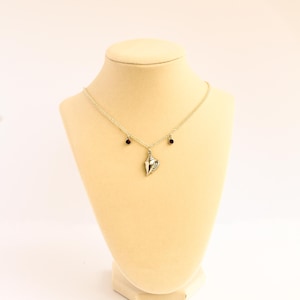 May include: A silver-toned necklace featuring a central seashell pendant suspended from a delicate chain. The chain is accented with two small, dark red circular beads positioned symmetrically on either side of the central shell charm.