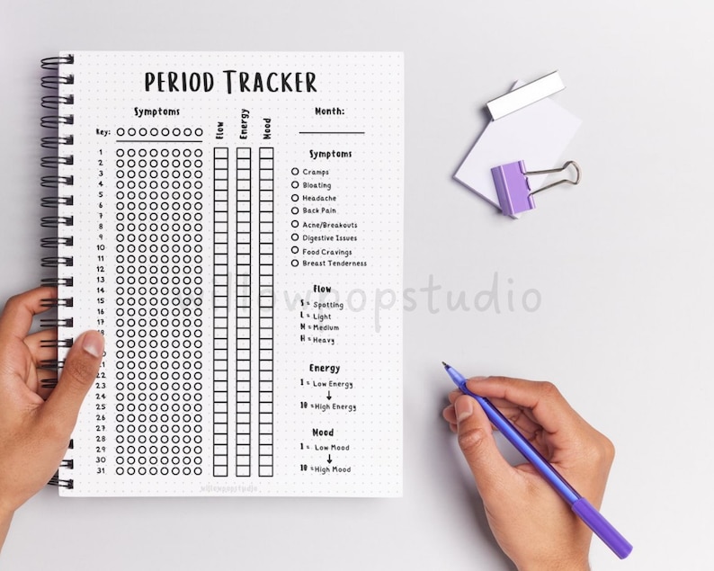 May include: A spiral-bound period tracker notebook with a white dotted page featuring a header that reads PERIOD TRACKER. The layout includes columns for symptoms, flow, energy, and mood, with a list of symptoms like cramps and bloating.