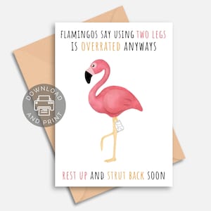 May include: A greeting card featuring a pink flamingo with a black beak and a leg in a cast. The card has text that reads "FLAMINGOS SAY USING TWO LEGS IS OVERRATED ANYWAYS" and "REST UP AND STRUT BACK SOON". The card is on a white background.
