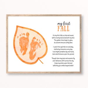 May include: A framed print featuring a large orange leaf illustration with two baby footprints inside. The text reads: my first FALL, followed by a poem about autumn. The design uses black and orange lettering on a white background.