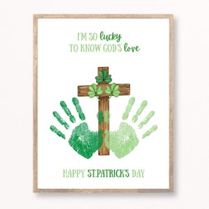May include: Framed print with a St. Patrick's Day design. It shows a wooden cross decorated with shamrocks, green handprints, and the text "I'M SO lucky TO KNOW GOD'S love" and "HAPPY ST.PATRICK'S DAY" in green.