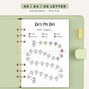 May include: A light green ring binder containing a Rate My Day printable page with a dotted grid, a star-shaped habit tracker numbered 1 through 31, and a colour-coded mood legend. The top text reads A5 | A4 | US LETTER and PRINTABLE + DIGITAL.